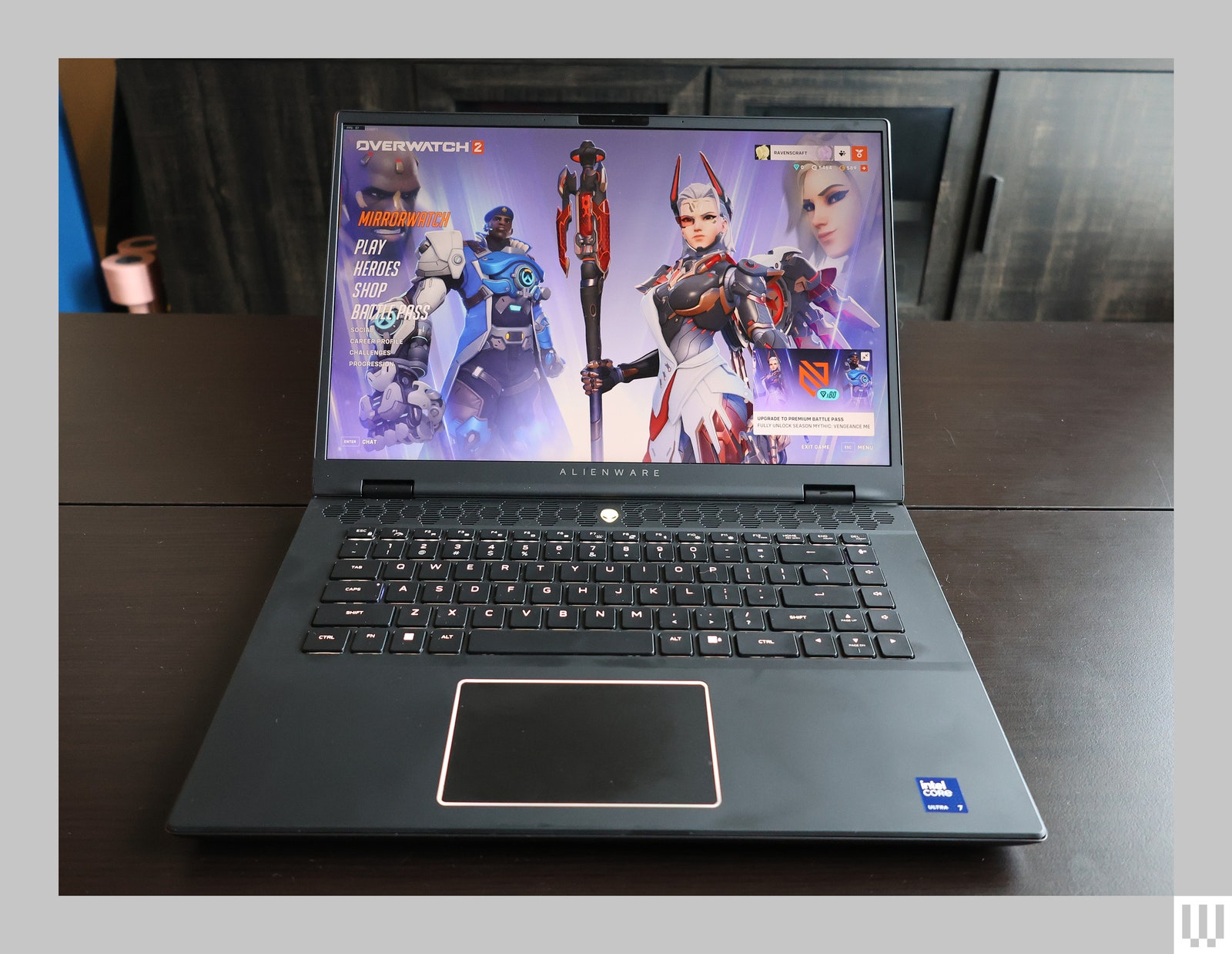 Black laptop opened and sitting on wooden surface with screen showing game characters