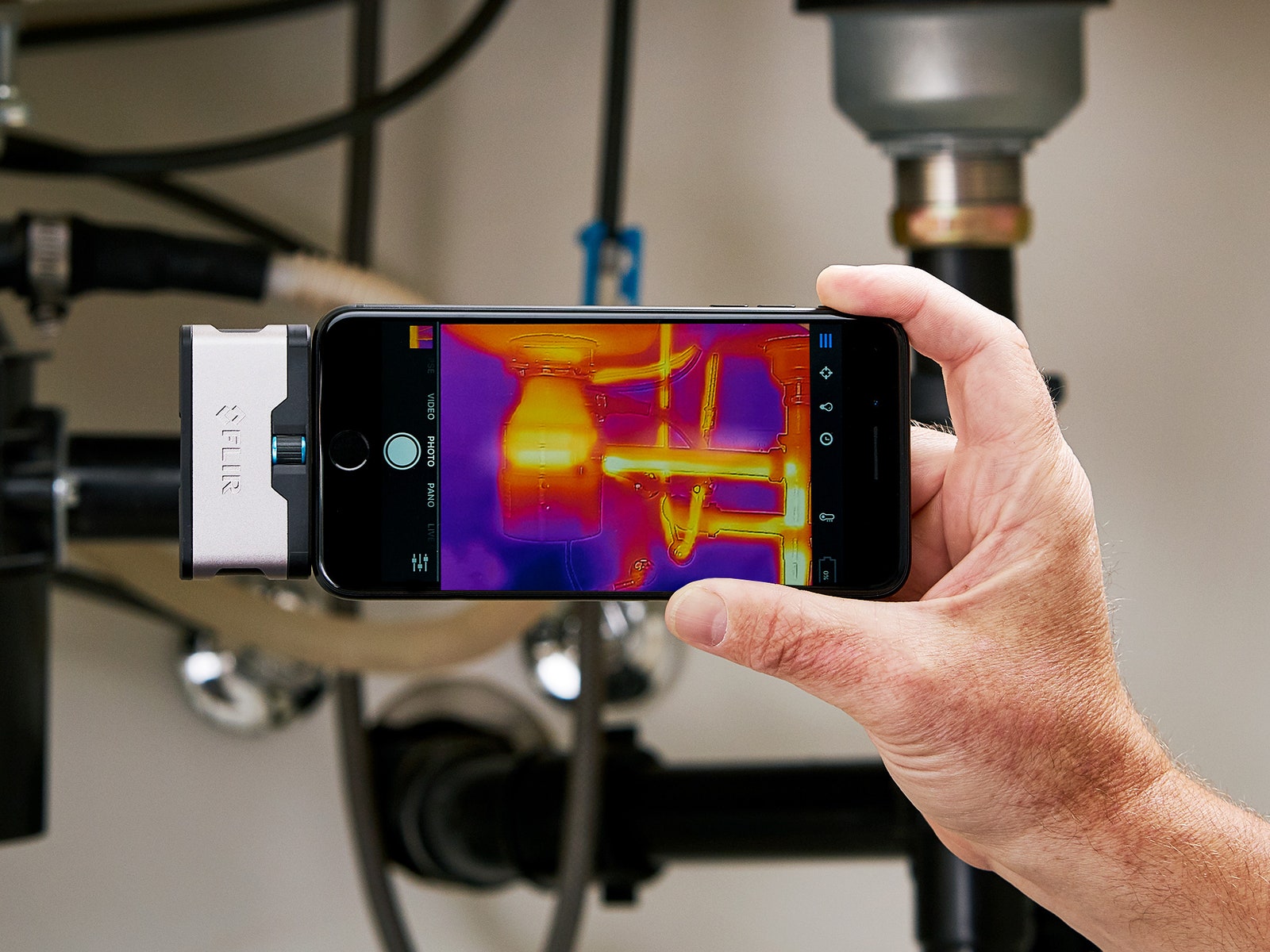 Person's hand holding up a smartphone with the Flir One Gen 3 thermal camera attachment.