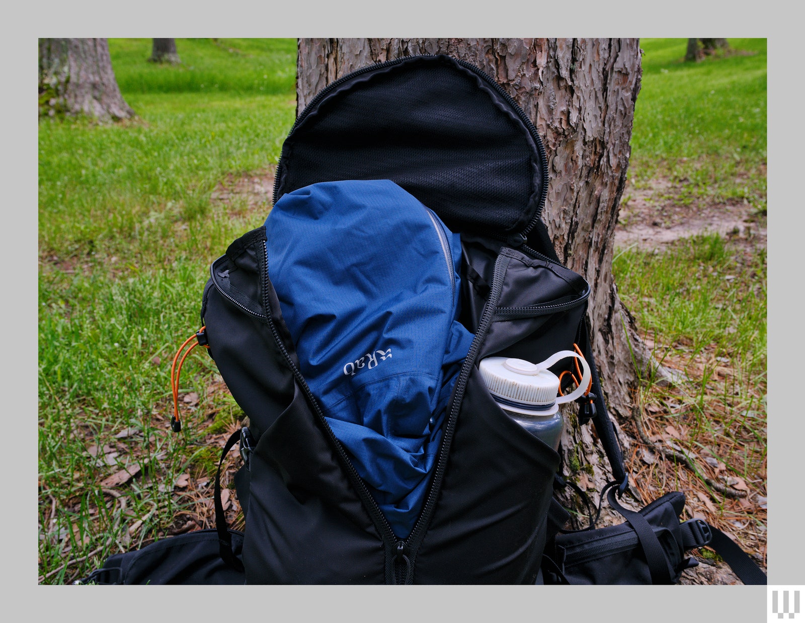 A partially opened black backpack with padded waist straps and a thick reusable water bottle in a side pocket leaning...