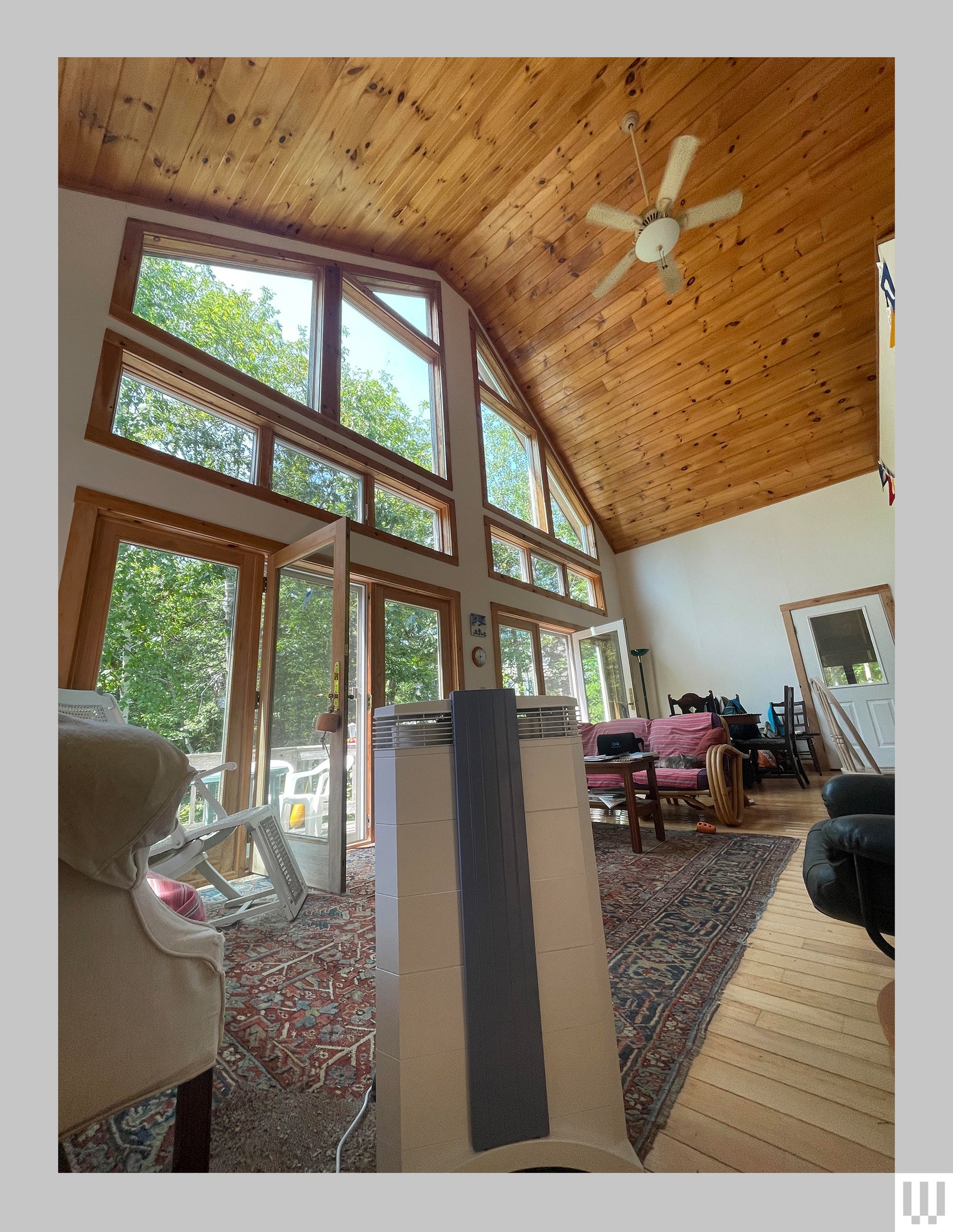 Rectangular air purifier on the floor of a room with high ceilings a wall of windows and ceiling fan