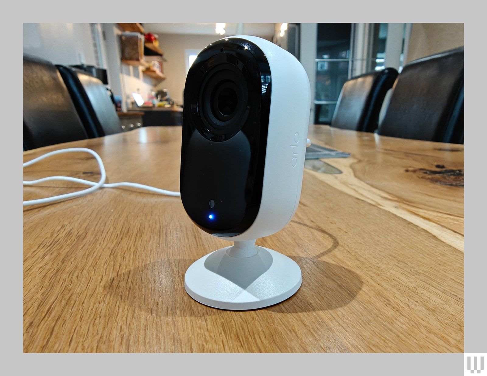 Oval shaped indoor security camera by Arlo with white base and black front sitting on wooden surface