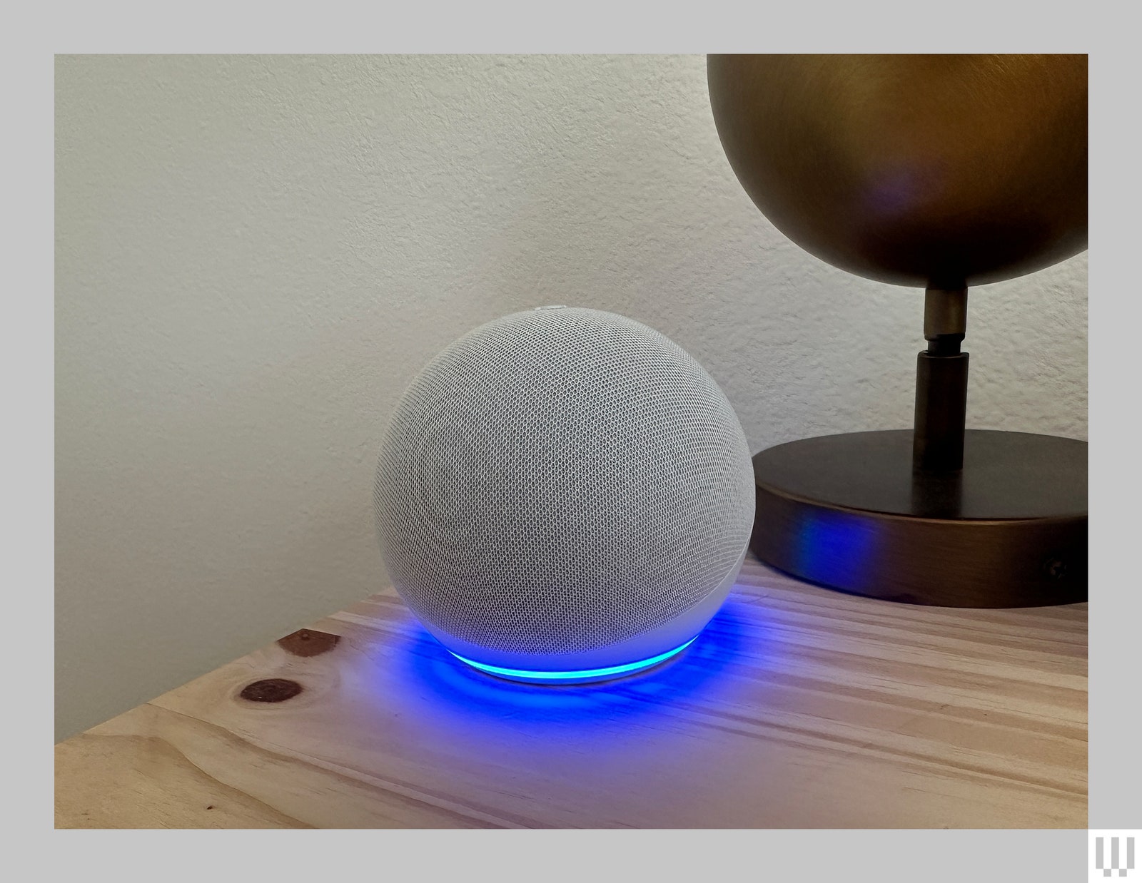 Grey sphere device with blue light illuminating from the base while sitting on a wooden nightstand