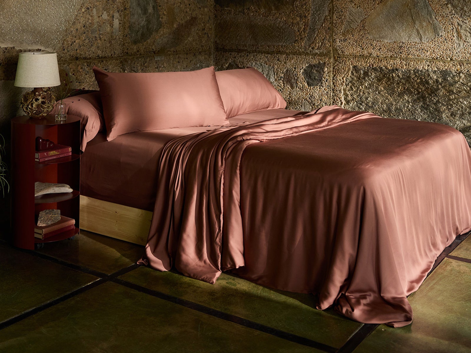 Brownish red colored sheets and pillowcases on a bed in a room with stone walls