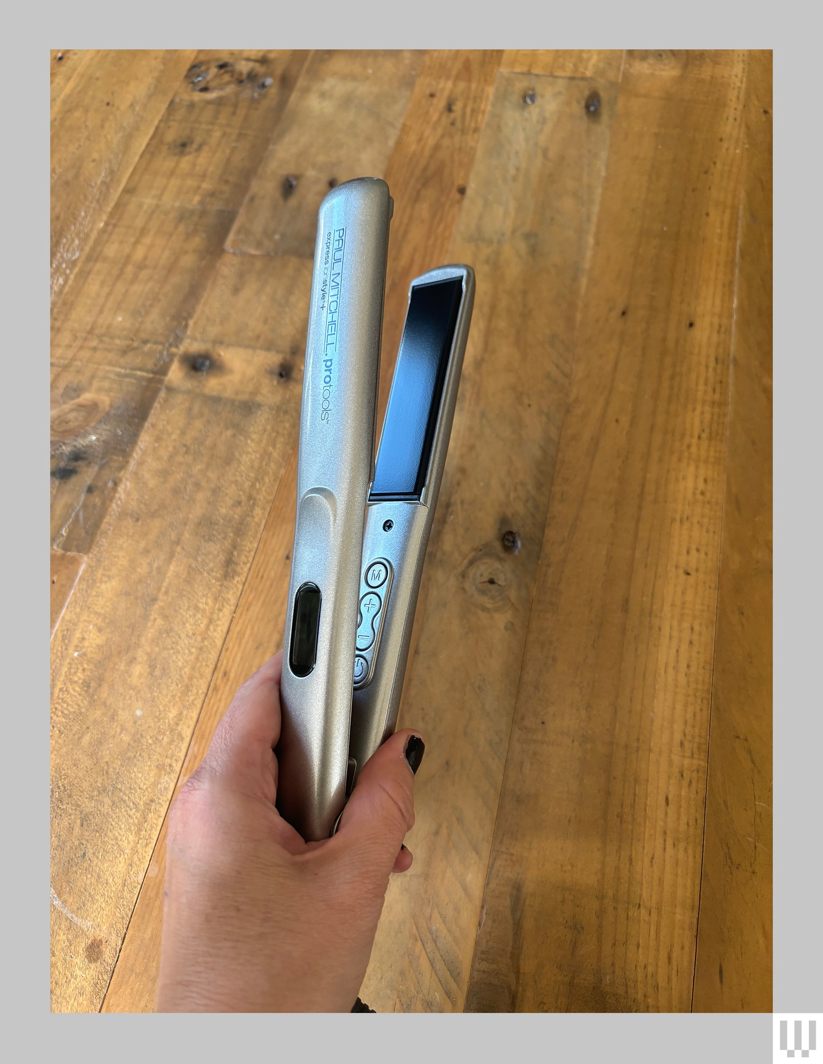 Hand holding a thin silver hair straightener showing a black colored panel on the inside of one of the clamps