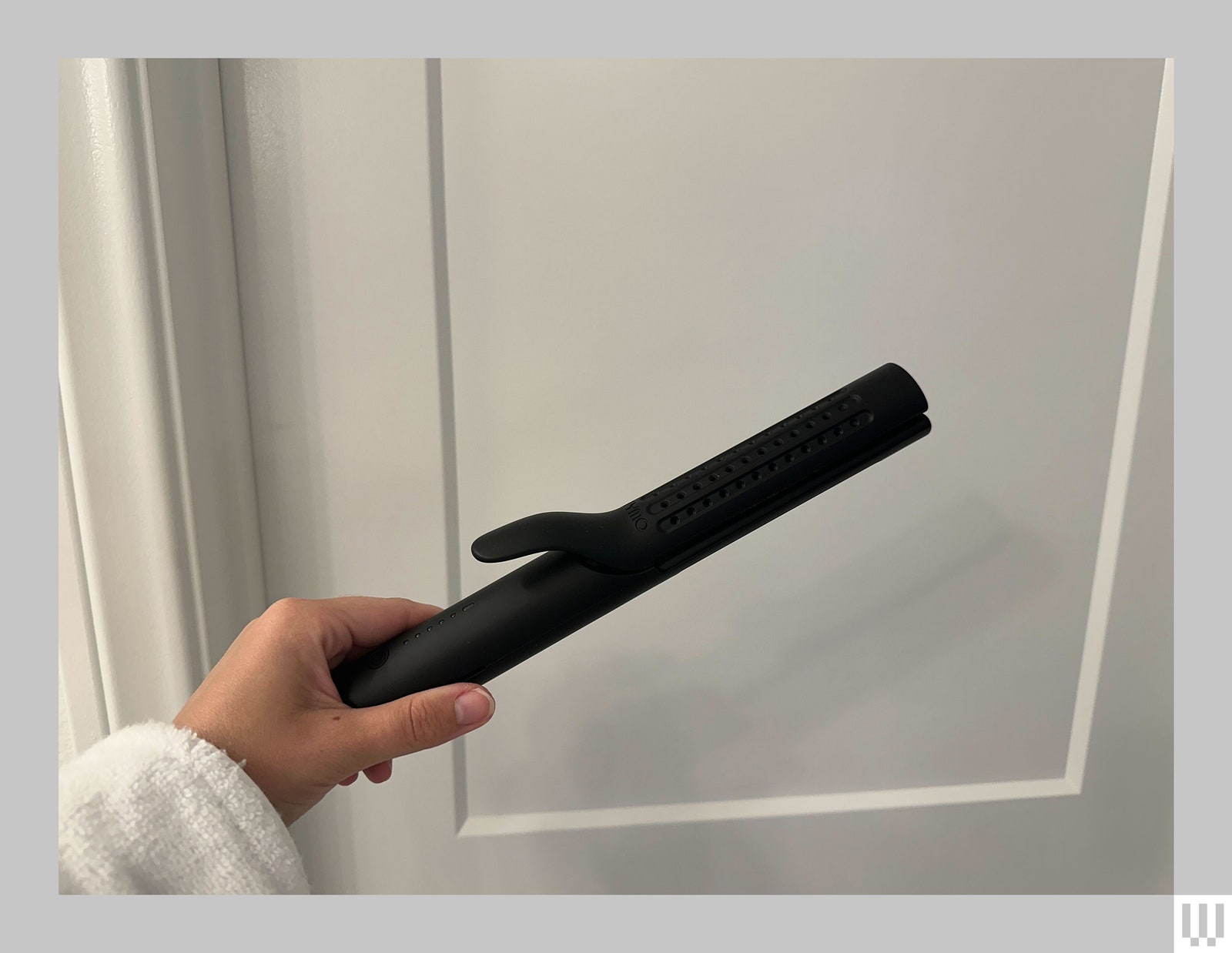 Hand holding a black hair straightener in front of a white all