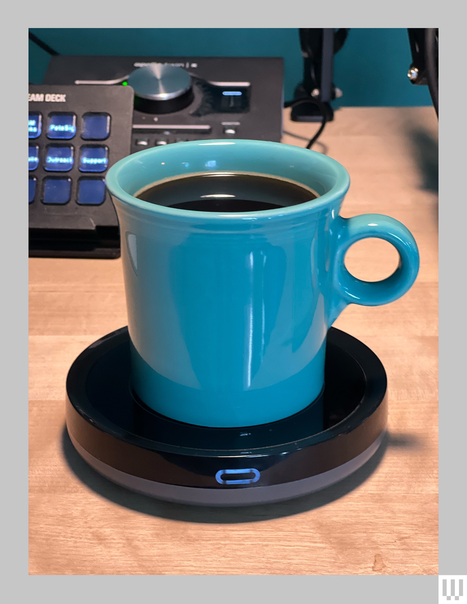 Black discshaped device under a teal mug with brown liquid inside keeping the drink warm