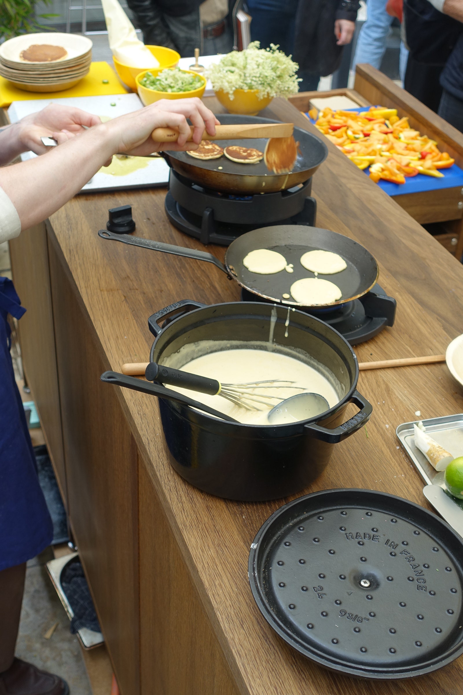 A person flipping mini pancakes with a stick with other kitchen prep on a counter