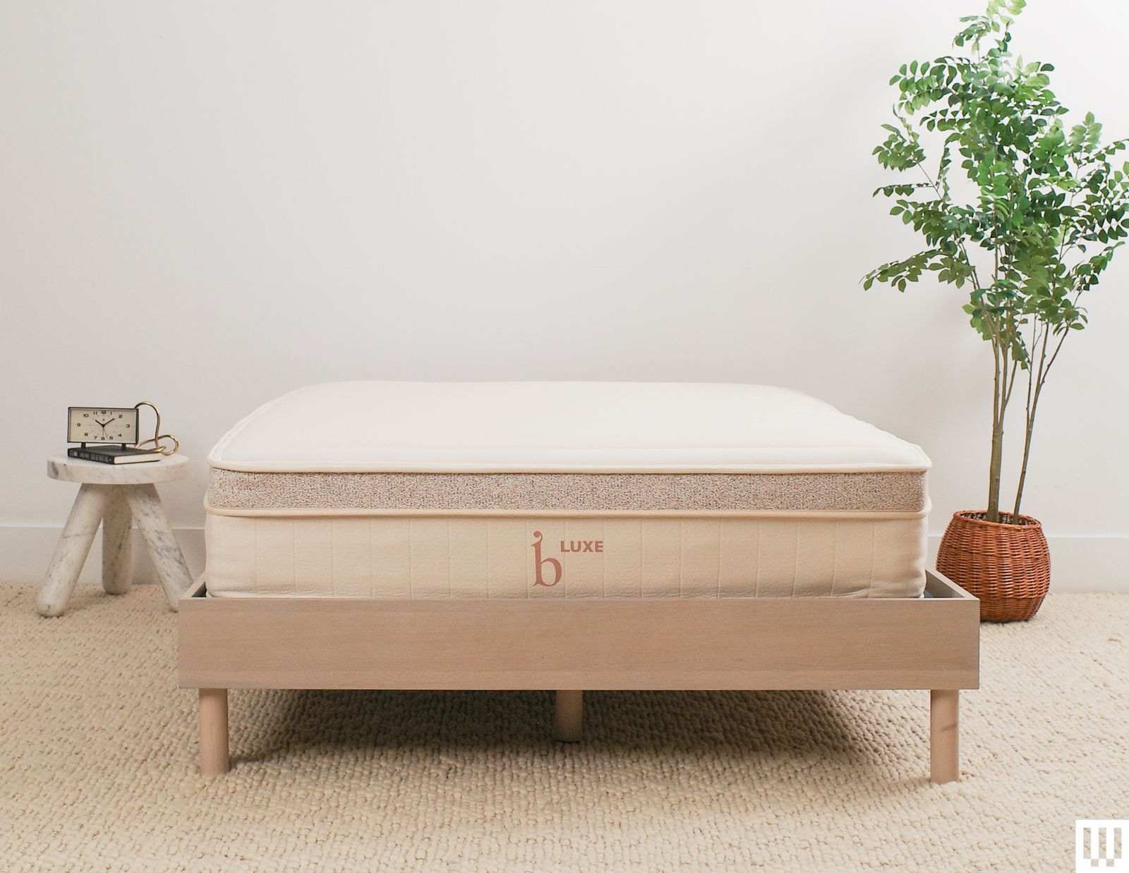 Birch Luxe Natural Mattress a white mattress with tan trim on a minimalist wooden frame with a nightstand and potted...