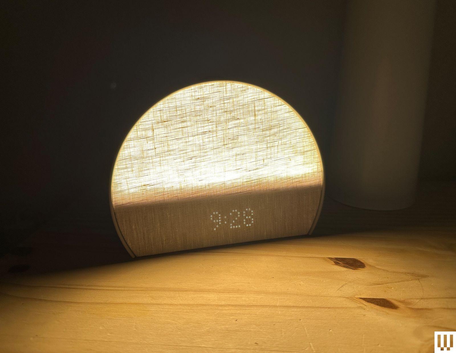 Hatch Restore 3 a semicircular shaped alarm clock with an illuminated linen textured front sitting on a wooden nightstand