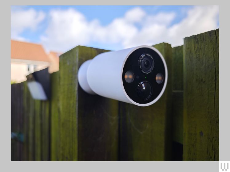 White cone shaped security camera with multiple lenses attached to wooden fence