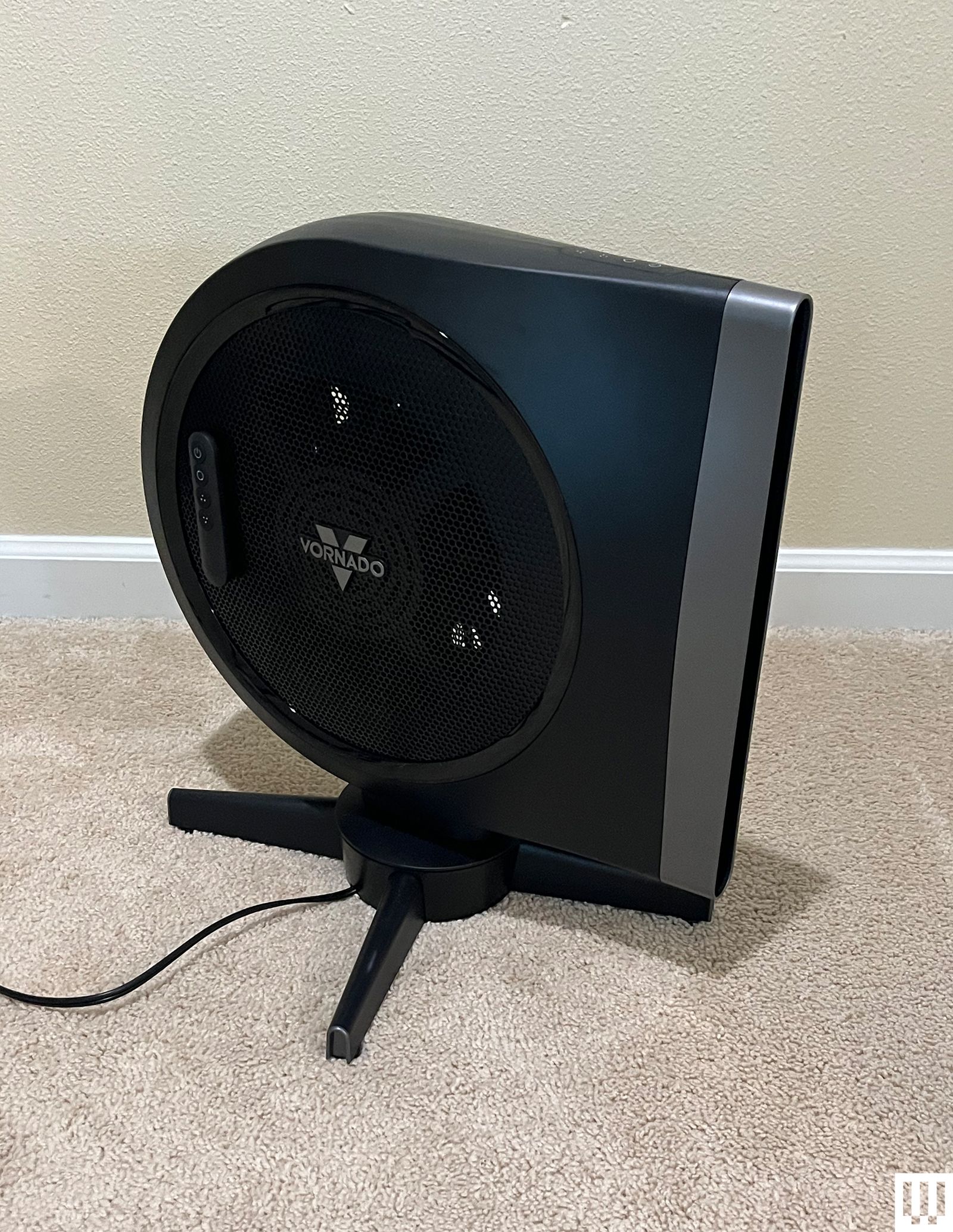 Vornado Strata a black fan sitting on a carpeted floor with a rounded left side and narrow right side