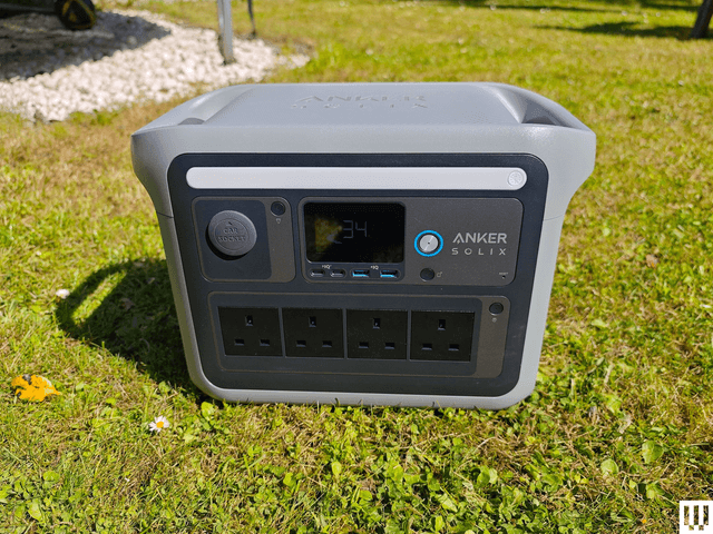 Grey square device sitting in the grass with large handles on each side and outlets, screens, and button the front