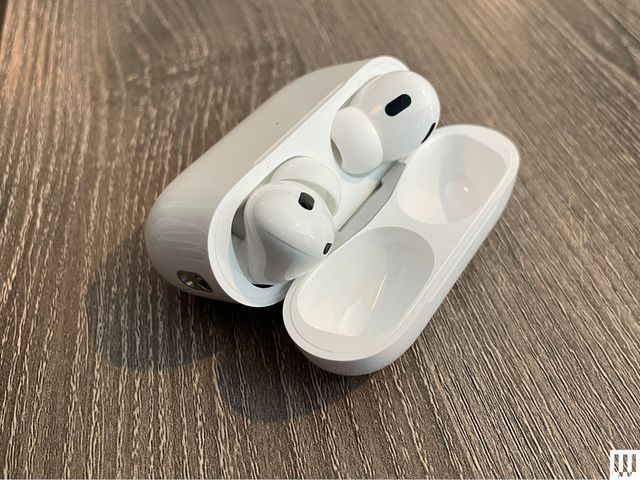 Apple AirPods Pro 2, two white earbuds, in an open oval shaped case sitting on a wooden surface