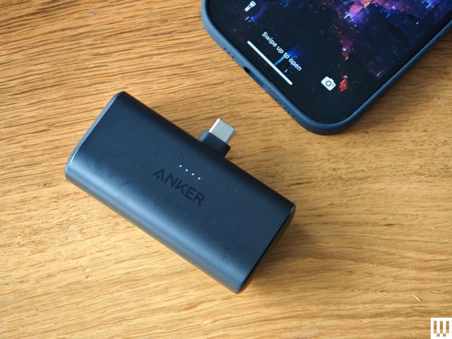 Anker Nano Power Bank, black rectangular device with a USB port on the side and another port on the top, sitting near the bottom of a mobile phone.
