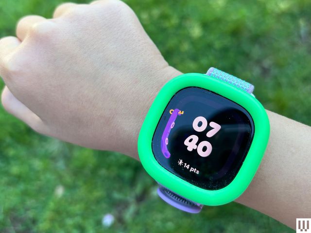 Child's wrist with a digital wristwatch and the screen showing the time and game points earned