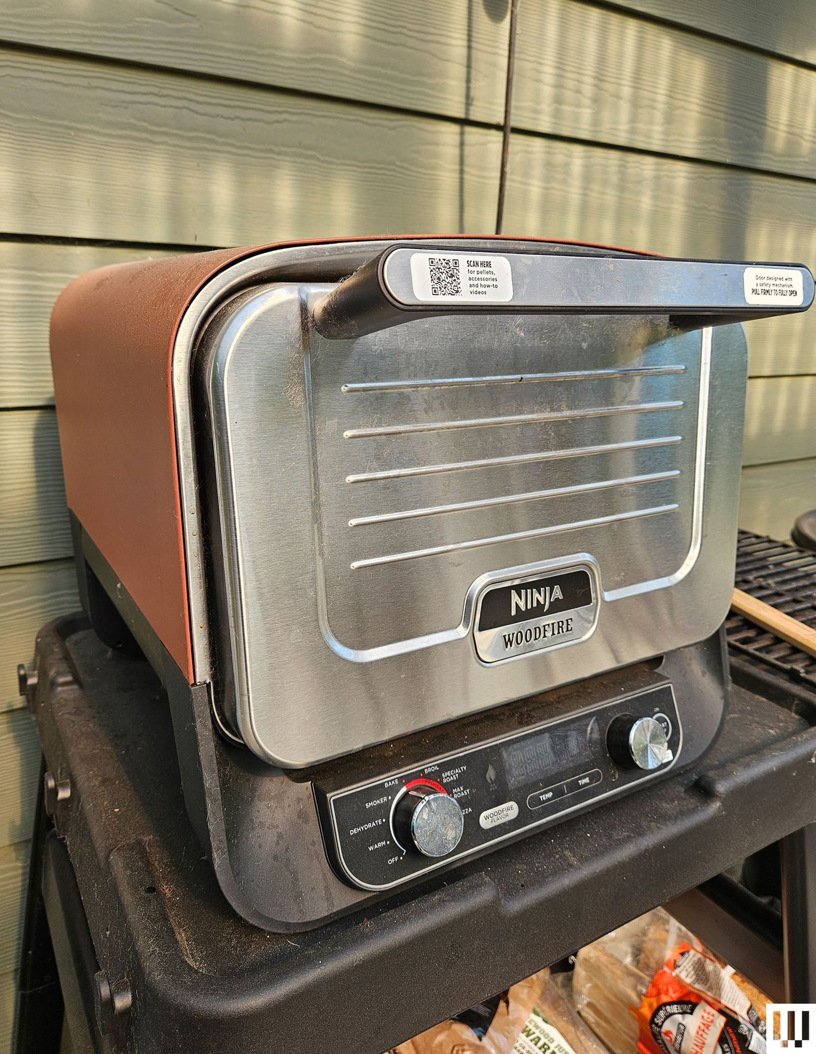 Small pizza oven sitting on a black shelf outdoors beside a house
