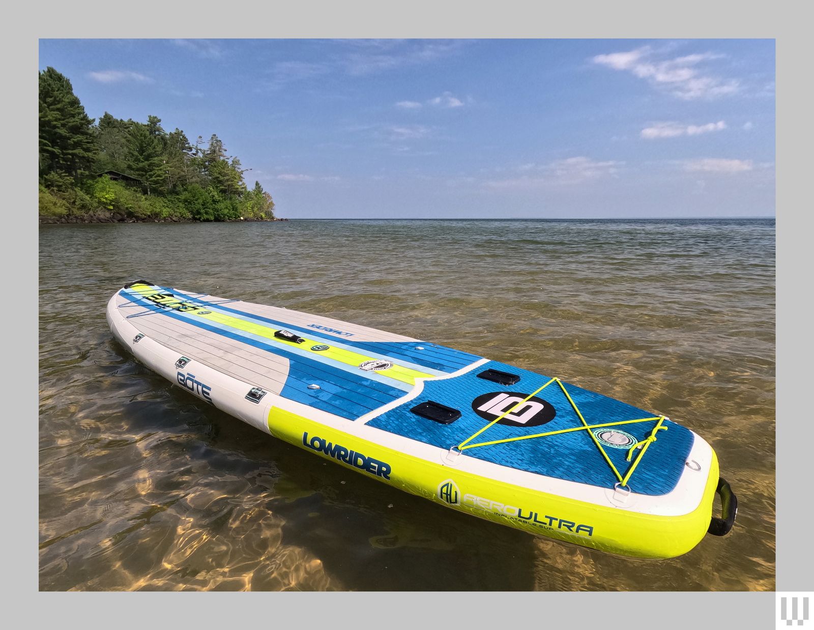 Long blue and neon green paddleboard floating in water with a piece of treefilled land jutting into the water in the...