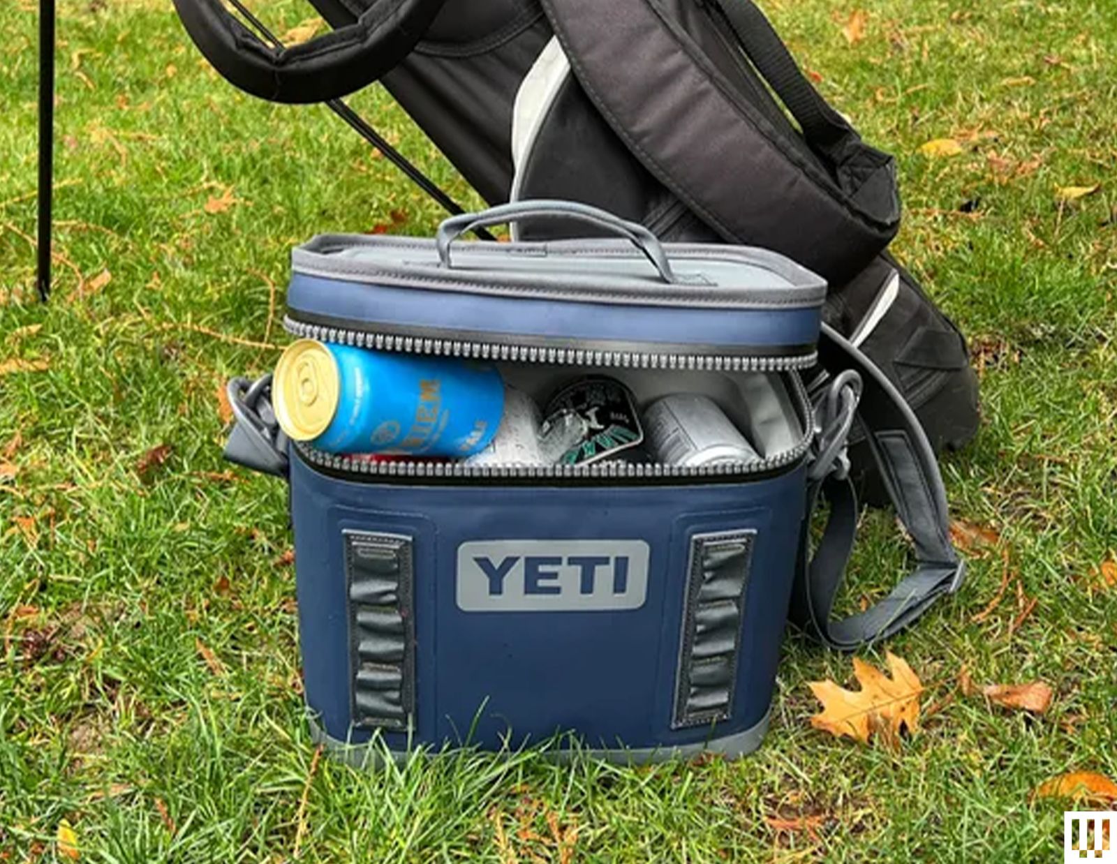Yeti Hopper Flip 8 Cooler a blue padded device holding canned beverages leaning against a black golf bag sitting in the...