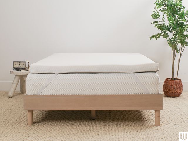 Helix Sleep GlacioTex Premium Mattress Topper, a thick pad laying on top of a white mattress sitting on a light brown minimalist bed-frame with a nightstand and potted plant on either side of the bed