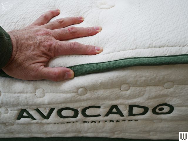 Closeup of a hand pushing down on an Avocado Green Mattress, showing the thick white side with green trim