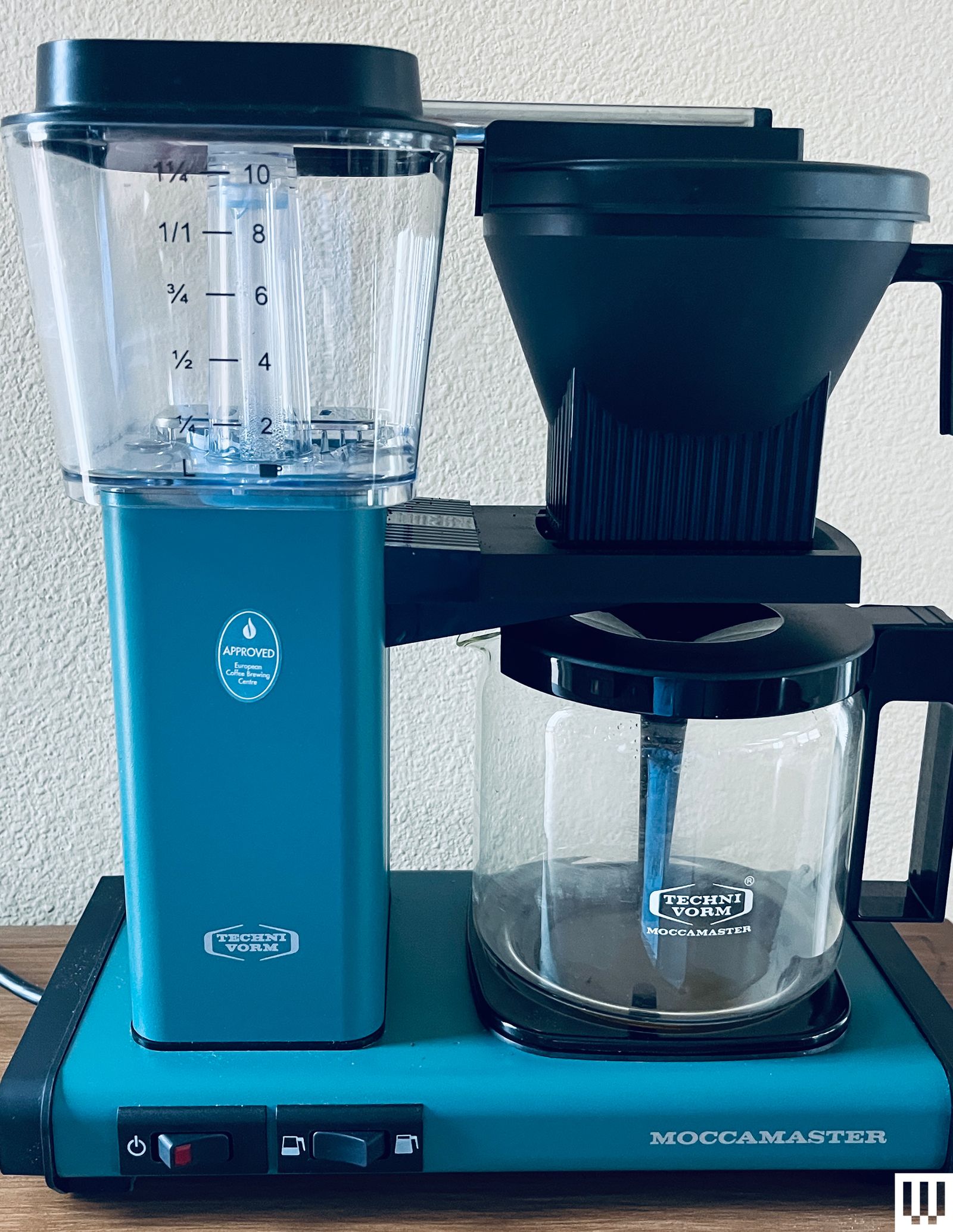 Front view of Moccamaster KBG.V. Select Coffee Maker in blue a raised clear container connected to a spout for coffee...
