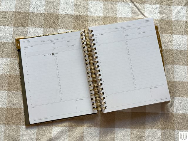 Overhead view of the Day Designer Daily Planner open on a beige and white checkered cloth, the inside pages showing blank to-do lists