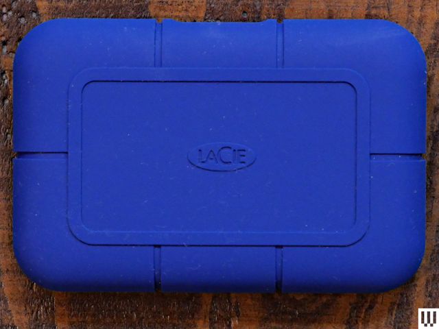 Overhead view of a LaCie Rugged SSD Pro5 external hard drive, a blue rounded rectangular device on a wooden surface