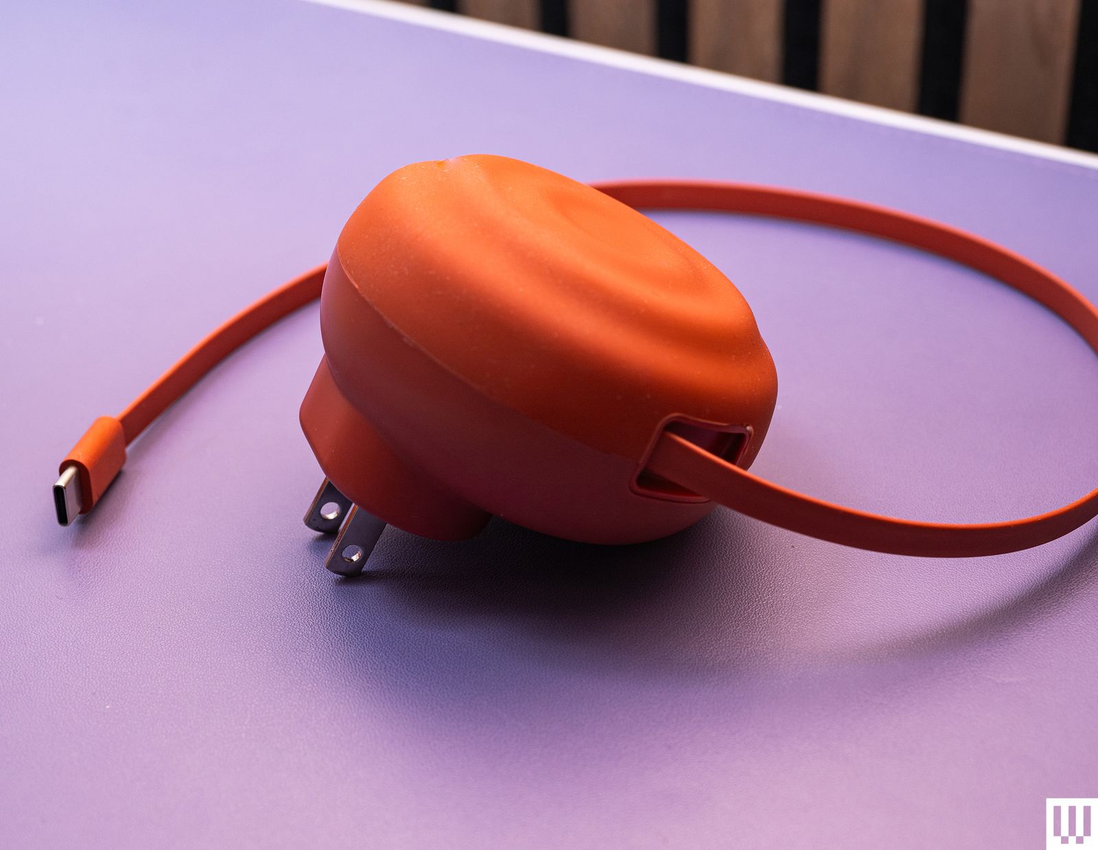 Counterpart the Charger in orange a discshaped shell with a retractable cord curled around it resting on a purple mat