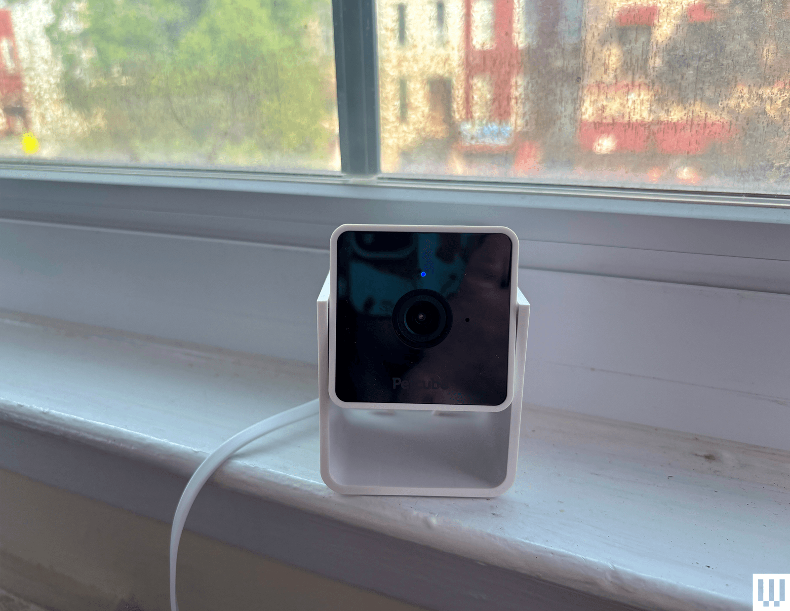 Square white pet camera with black screen sits on a white window sill.
