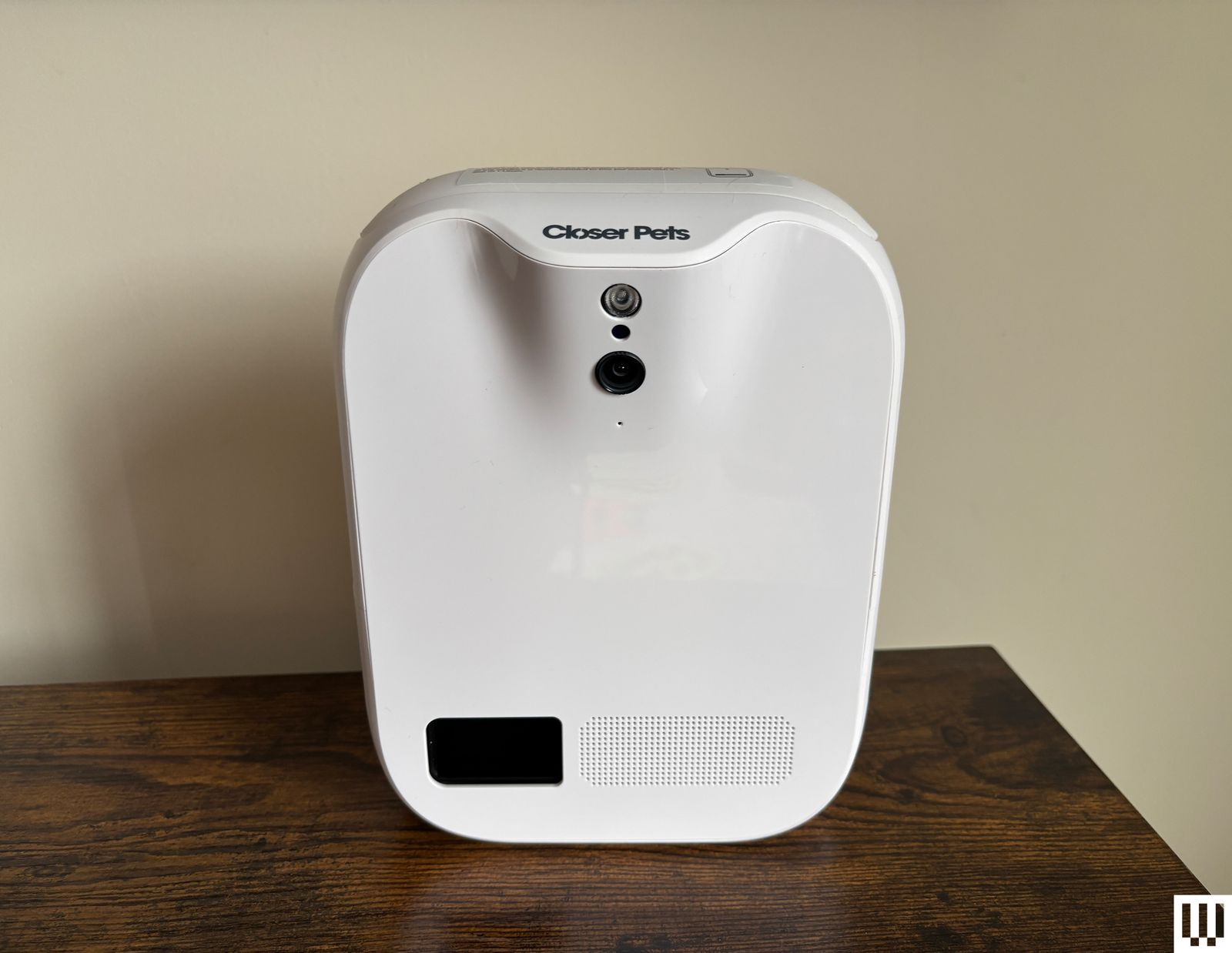White rectangle treatdispensing pet camera sits on a wood ledge with cream wall background