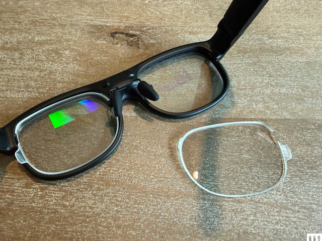 A pair of black smart glasses with a prescription lens beside it