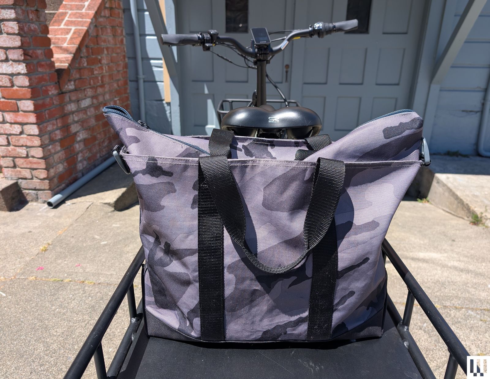 Large tote bag with purple and grey camouflage pattern on top of the back rack of a bike