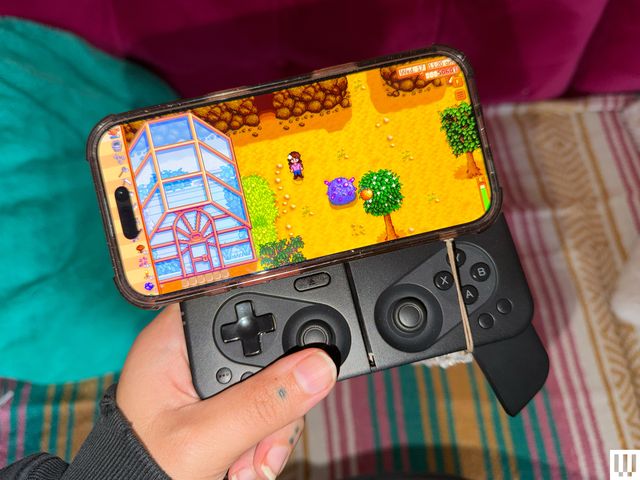 Hand holding a mobile gaming controller with a phone attached and the screen on to show a role-playing game