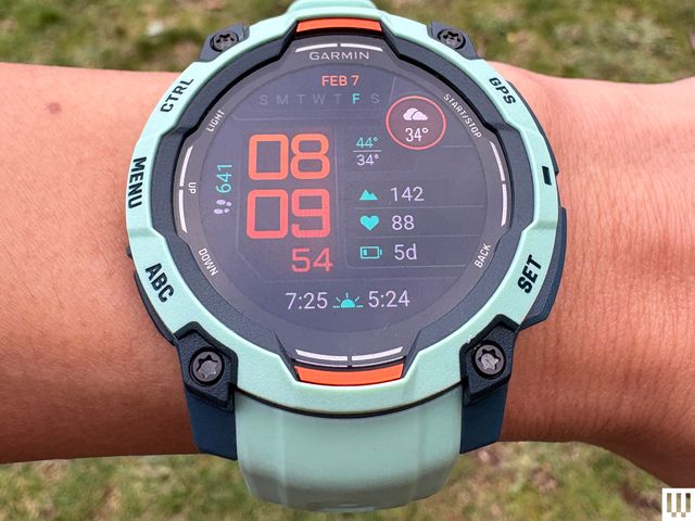 Overhead view of a wrist wearing a Garmin Instinct 3, a wristwatch fitness tracker with teal design and large digital display